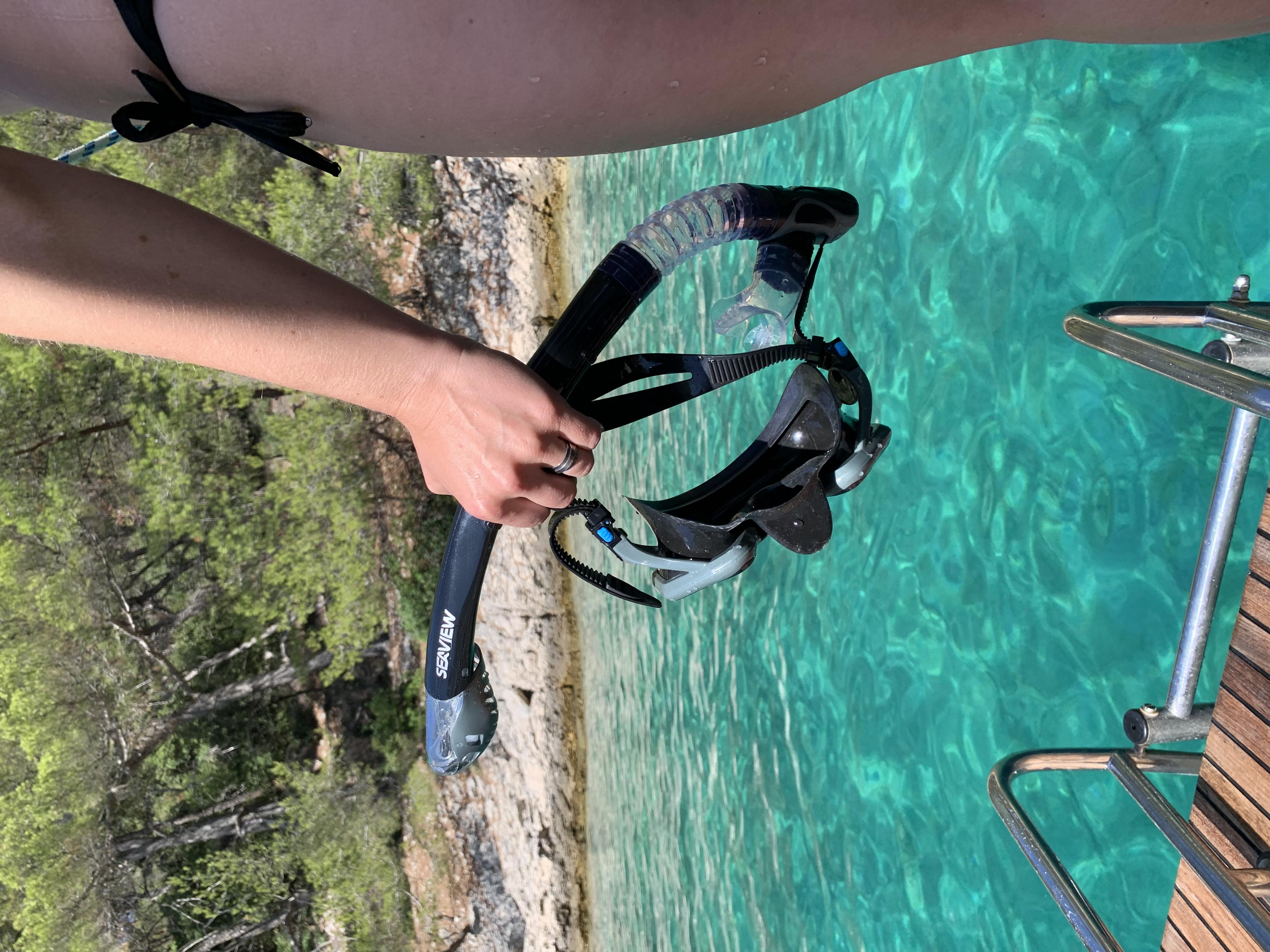 becky holding kradan snorkel set near water's edge