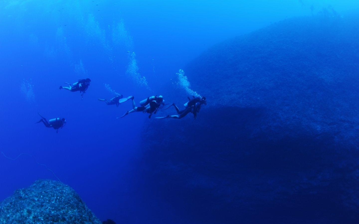 group of divers descending on rock structure